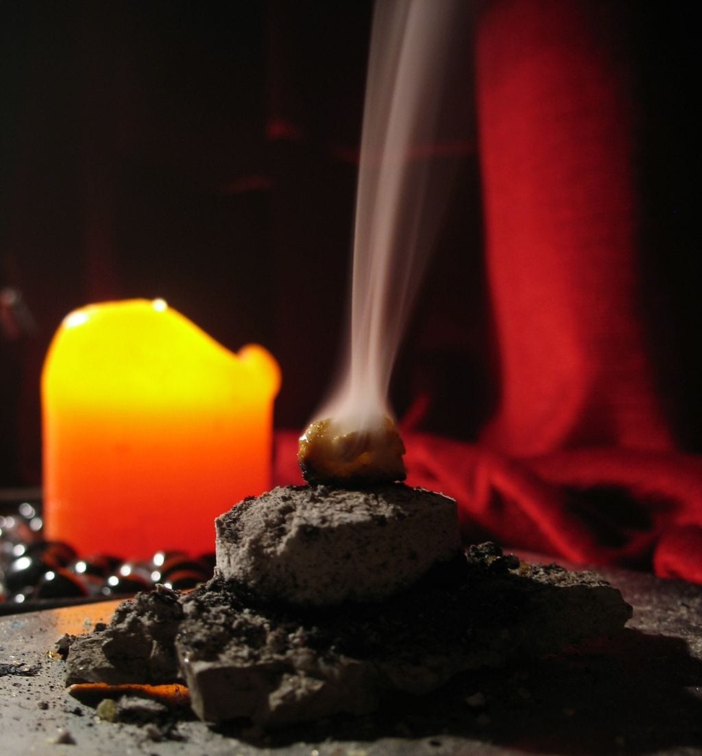 Photo of frankincense burning on coal. A candle burns in the background
