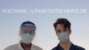 Click image to view video. Medical students in masks against a blue sky with video title text, "Stay Inside: A Toast to the Frontline", over their heads.