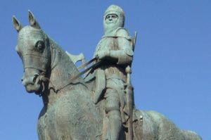 Robert the Bruce in battle armor on horseback. He is depicted wielding an axe and staring out into the distance, and the statue has gone green from oxidation. For article on Robert the Bruce leprosy