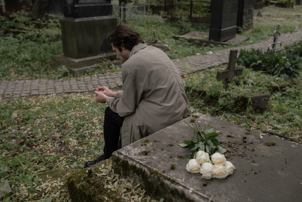 Man sitting by grave with flowers