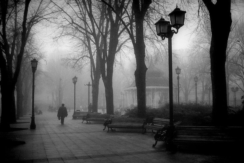 A foggy plaza in black and white, where one man is walking.
